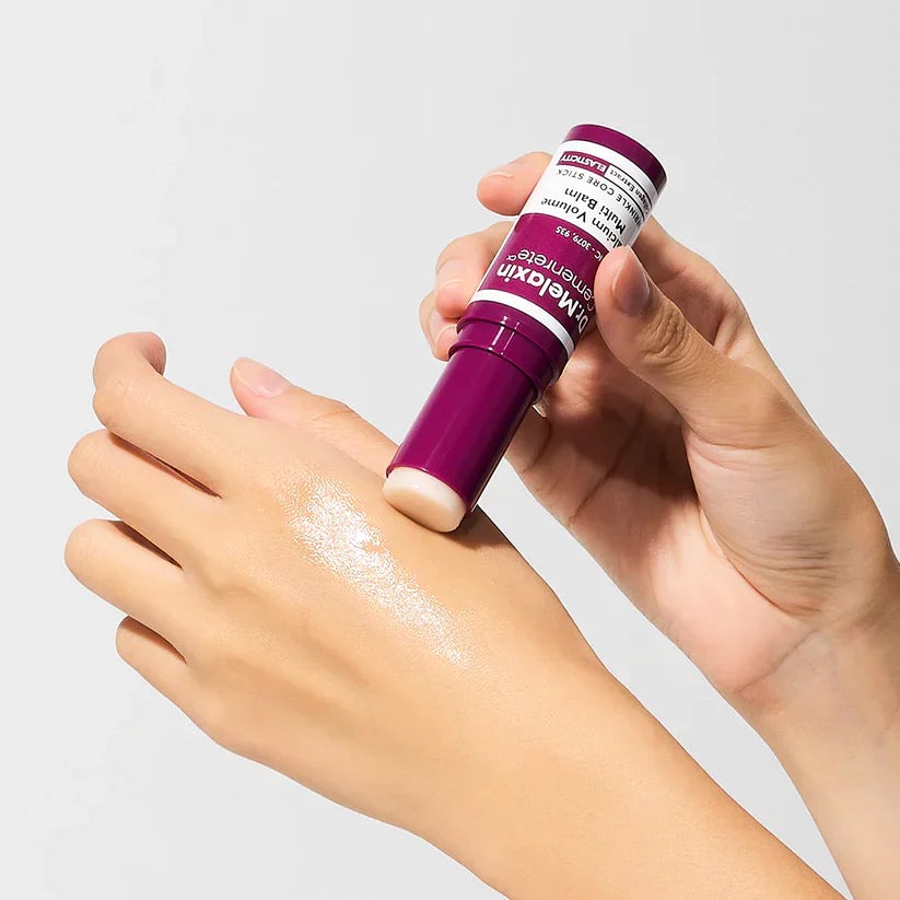 Hand swiping the Multi-Balm across the back of a hand, on a grey background